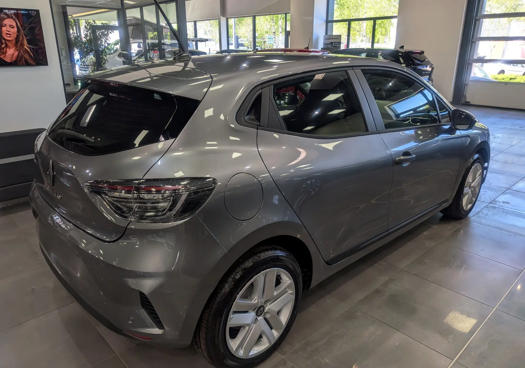 Vue 3/4 arrière droite d'une Renault Clio V gris schiste exposée en showroom, mettant en valeur ses feux arrière et jantes modernes.