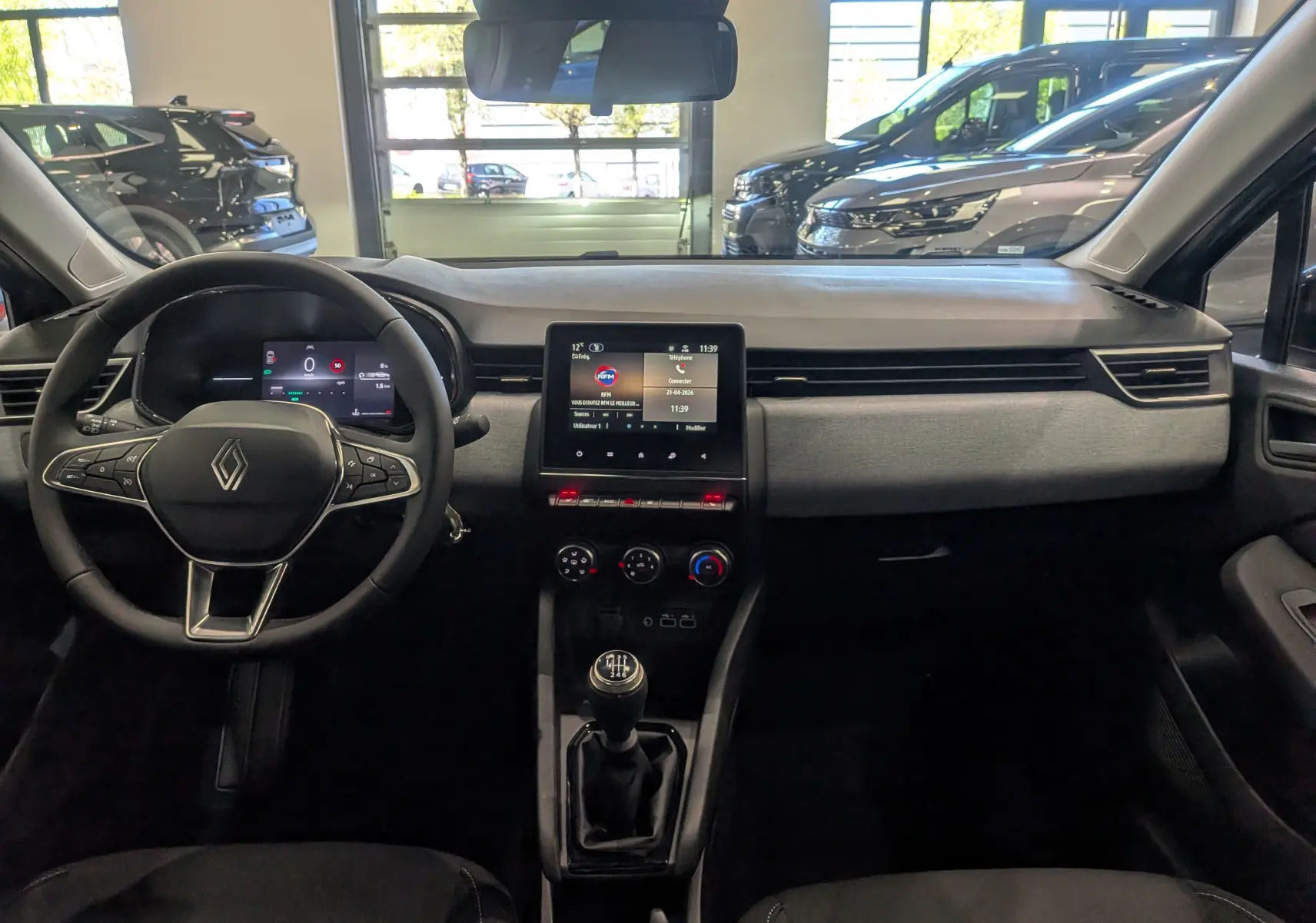 Vue intérieure frontale du tableau de bord de la Renault Clio V gris schiste avec écran tactile et boîte manuelle.