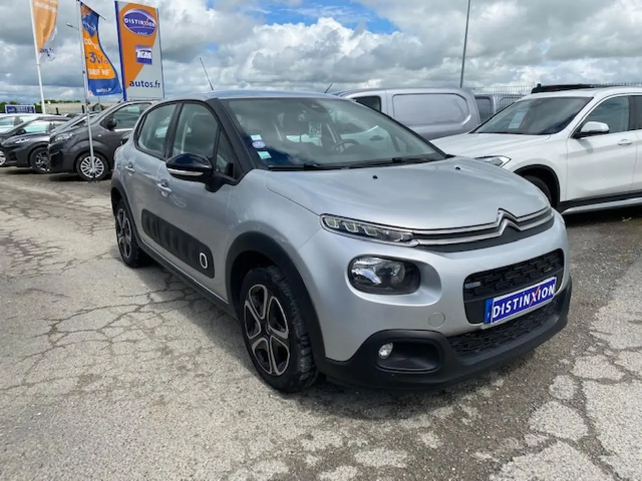 Citroën C3 gris clair vue 3/4 avant droit, avec protections latérales noires et jantes stylisées.