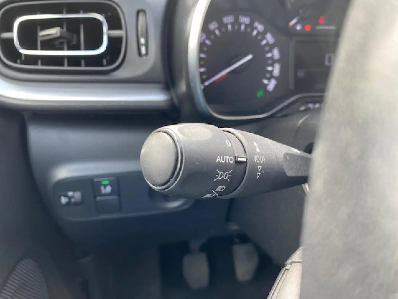 Gros plan sur la commande des phares automatiques à gauche du volant dans l'habitacle d'une Citroën C3 gris clair.
