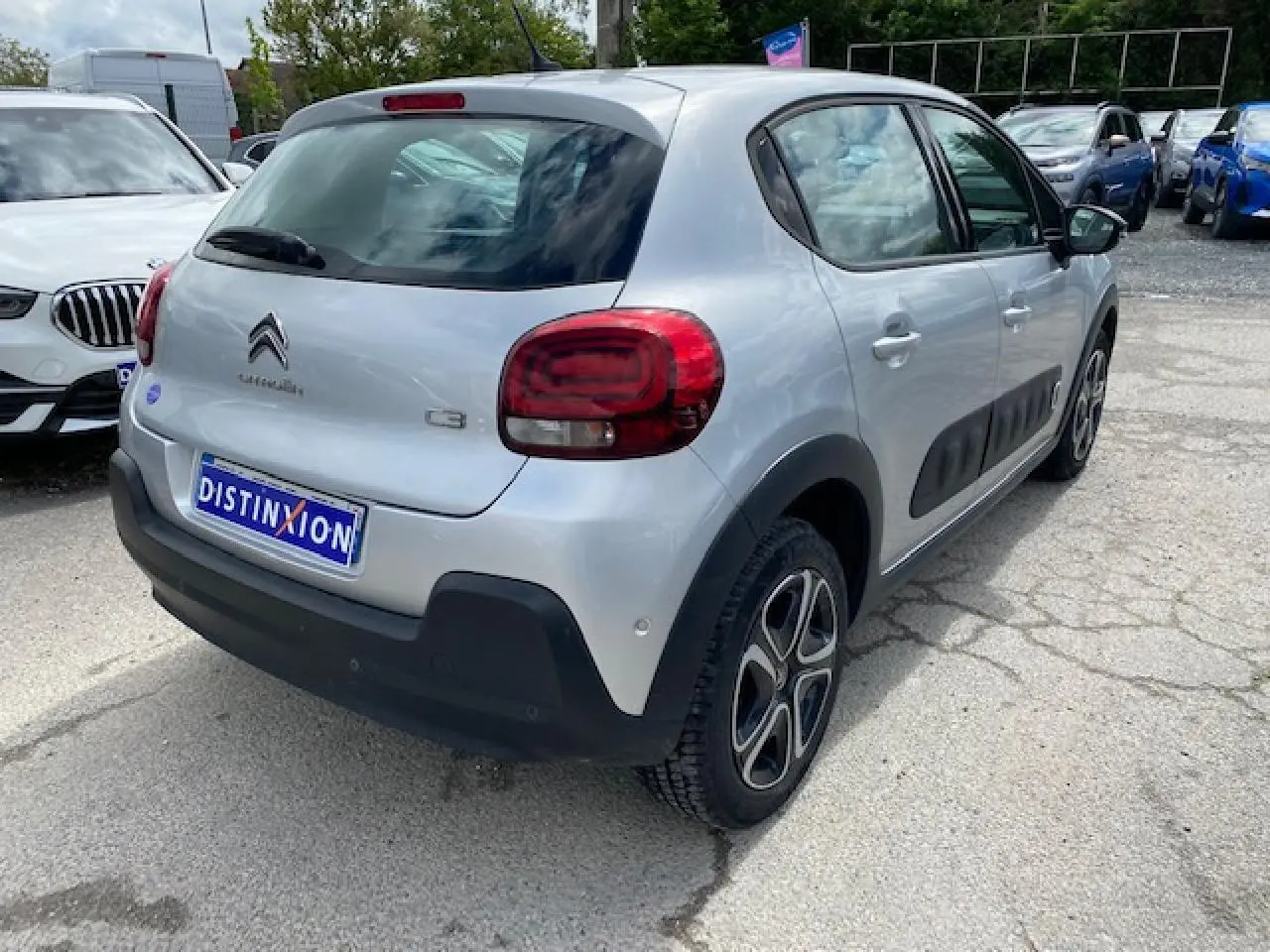 Vue 3/4 arrière droite d'une Citroën C3 gris clair avec enjoliveurs 3D et protections latérales noires.