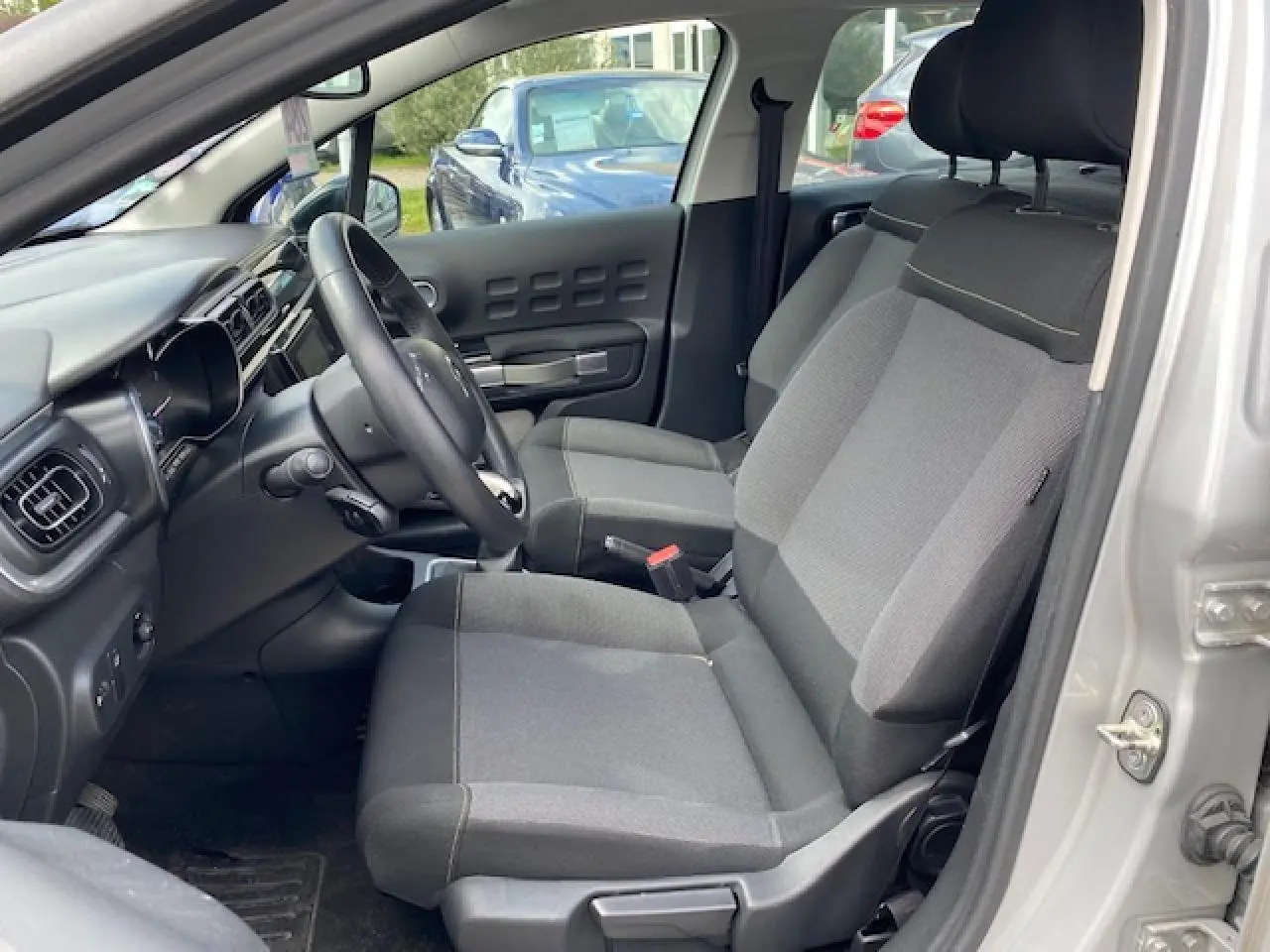 Vue intérieure côté conducteur de la Citroën C3 gris clair, montrant les sièges en tissu Mica Grey et le tableau de bord.