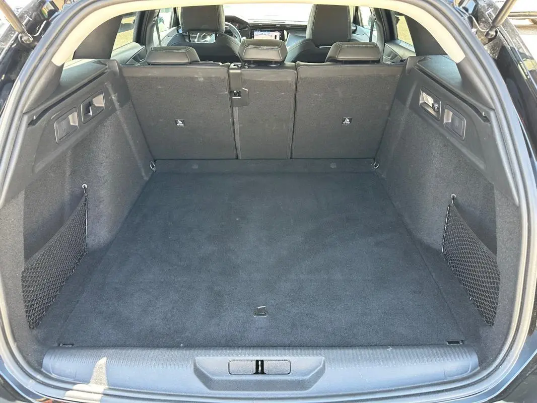 Coffre ouvert vu de l’arrière d’une Peugeot 308 SW Hybrid noire, montrant un espace de chargement propre et spacieux.