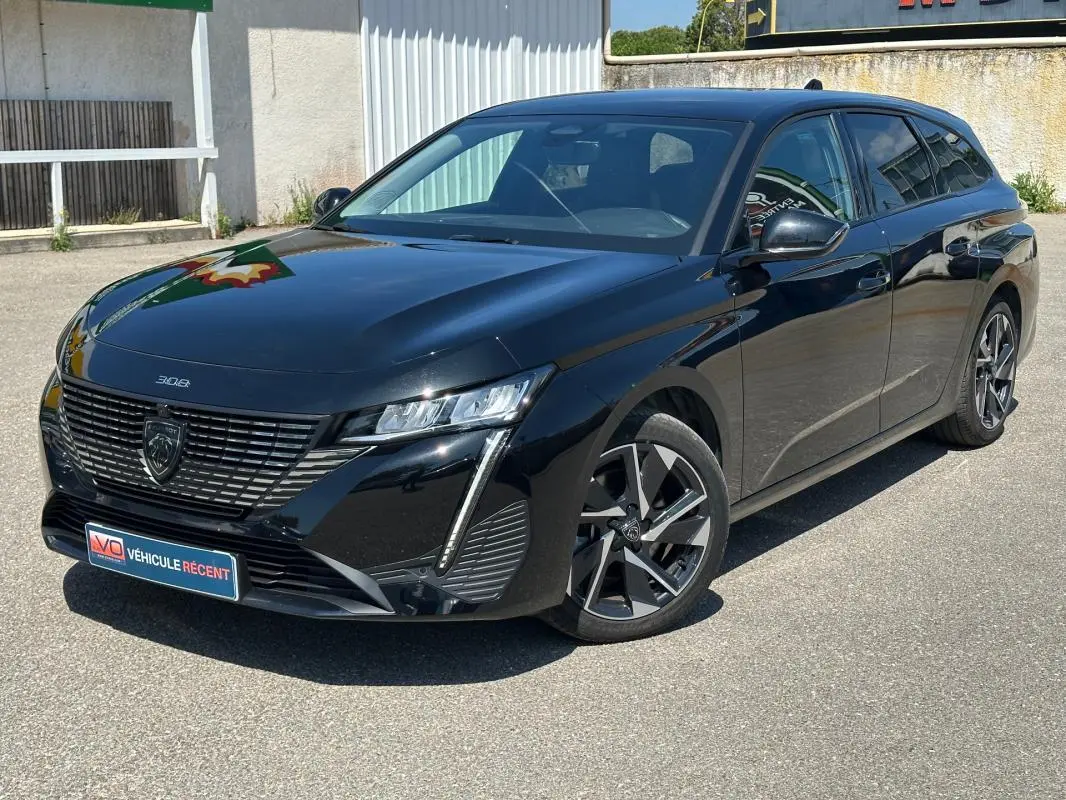 Peugeot 308 SW Hybrid 145 noir vue 3/4 avant droit, avec calandre distinctive et jantes alliage modernes.