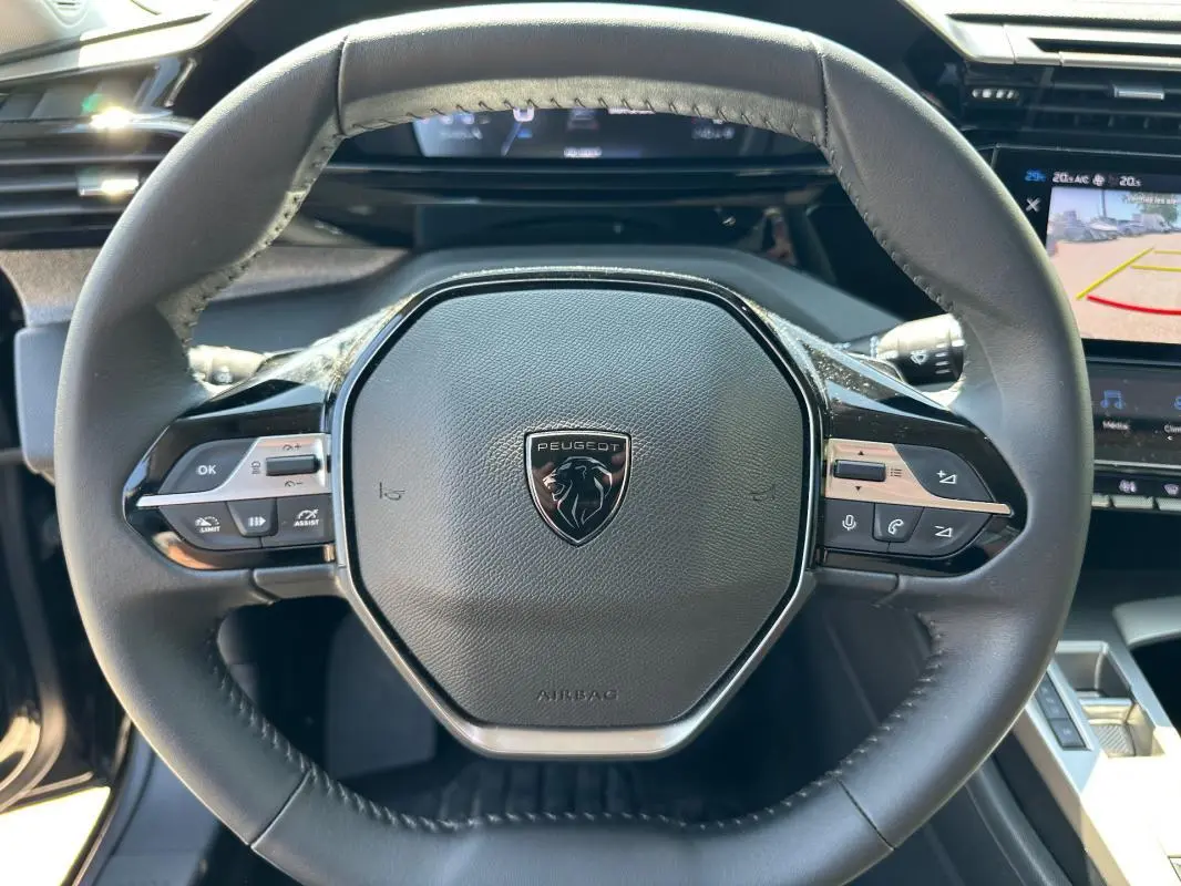 Vue rapprochée du volant noir du Peugeot 308 SW Hybrid 145 e-DCS6 Allure 2025 avec commandes intégrées et logo central.