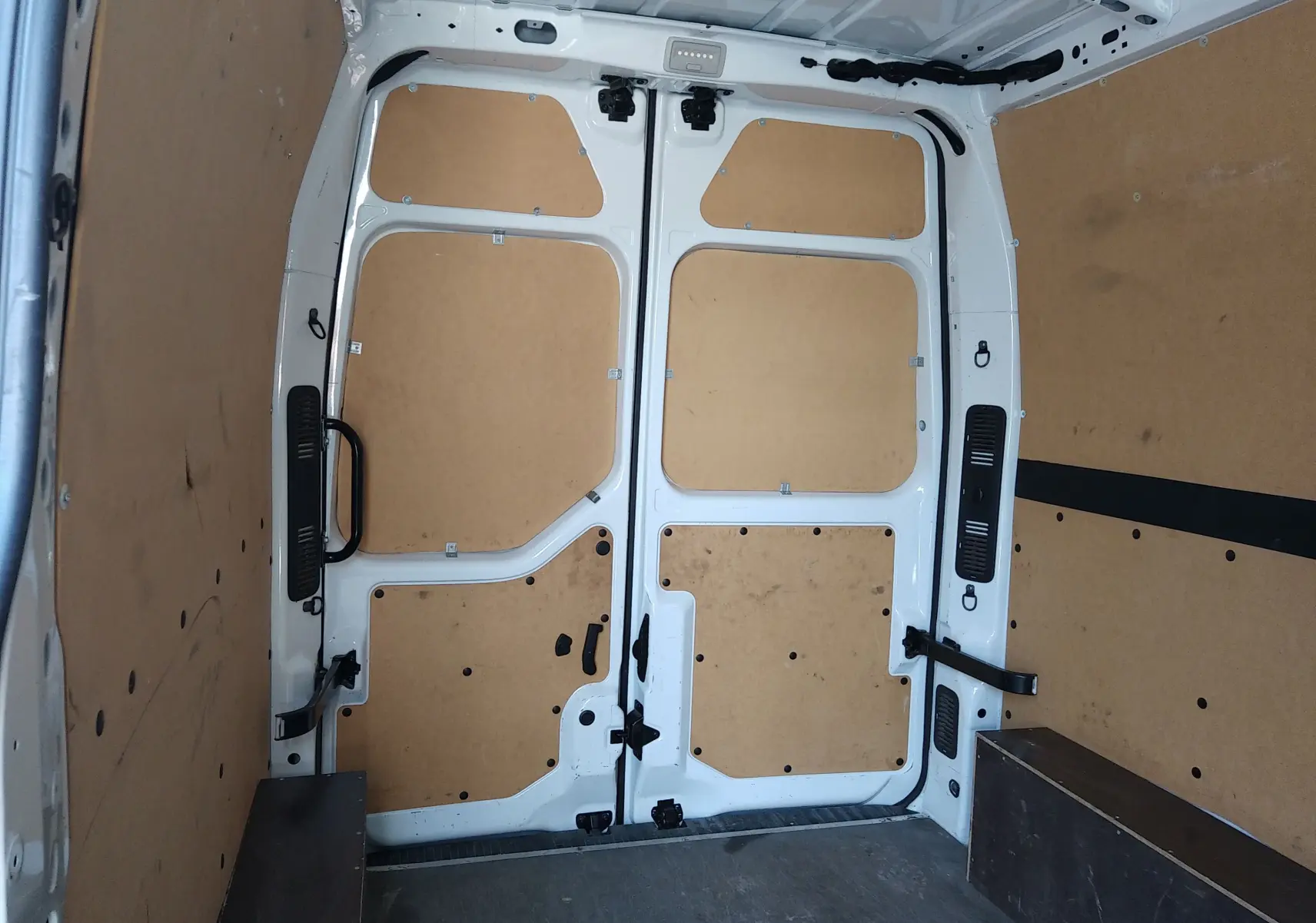 Intérieur du coffre d’un Renault Master blanc, vue arrière montrant les portes ouvertes avec habillage bois clair.