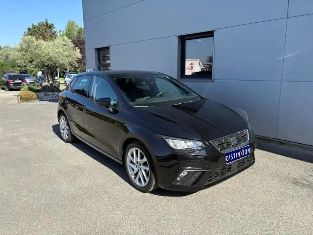 SEAT Ibiza 1.0 TSI 95 FR noire vue en 3/4 avant, stationnée devant un bâtiment gris par temps ensoleillé.