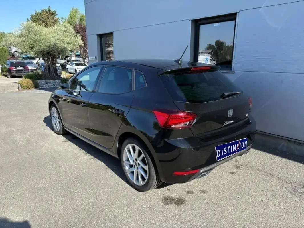 Vue 3/4 arrière droite d'une SEAT Ibiza noire garée devant un bâtiment avec jantes alliage visibles.