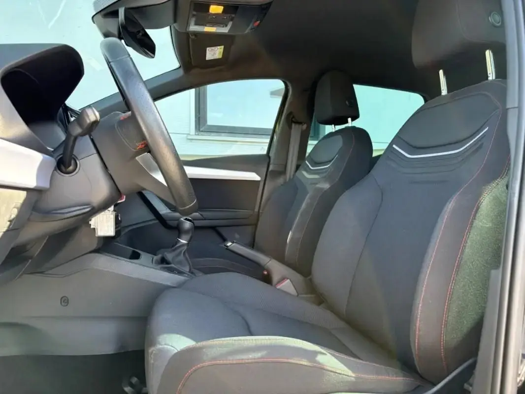 Intérieur de la SEAT Ibiza 1.0 TSI 95 FR 2025, vue côté conducteur montrant sièges noirs avec surpiqûres rouges.