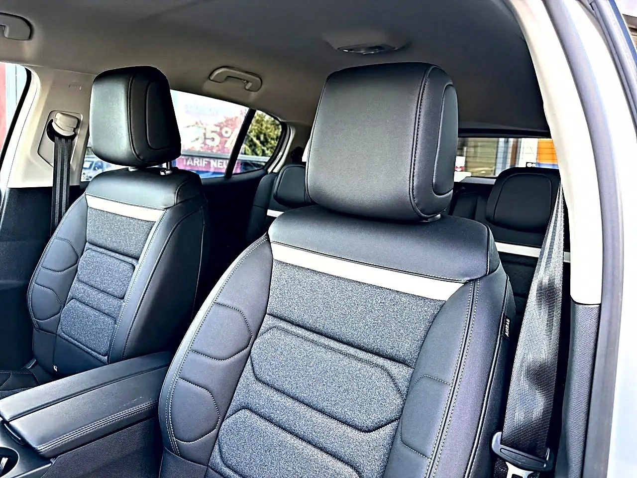 Vue intérieure côté avant droit du Citroën C5 Aircross 2025 blanc, sièges en cuir et tissu noir avec accoudoir central.