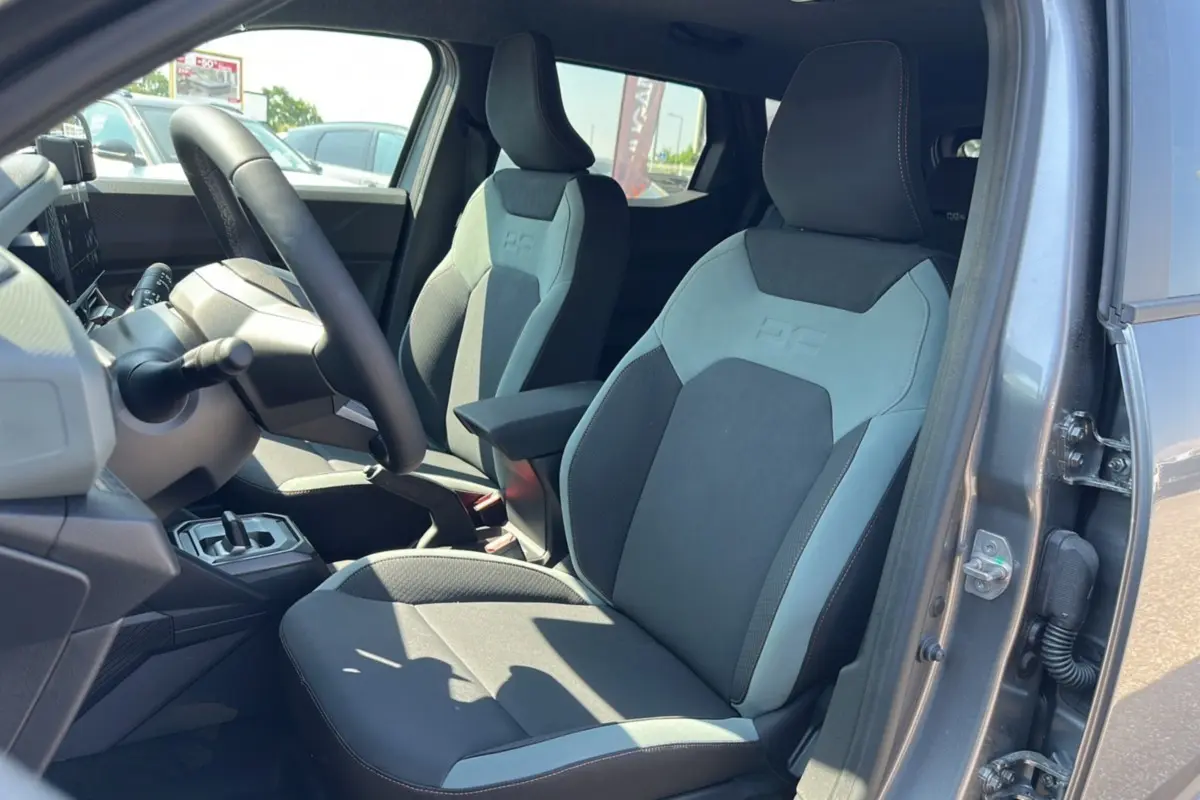 Vue intérieure côté conducteur du Dacia Duster 2025 gris schiste, mettant en valeur les sièges bi-matière avec logo HEV brodé.