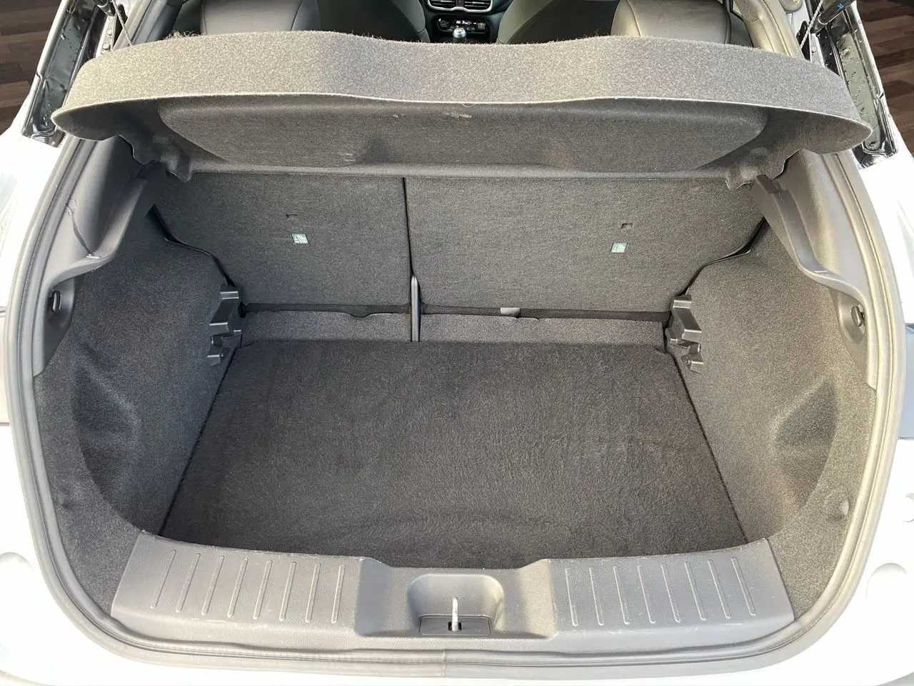 Coffre ouvert vu de l'arrière d'un Nissan Juke 2025 gris perle avec intérieur de coffre noir.