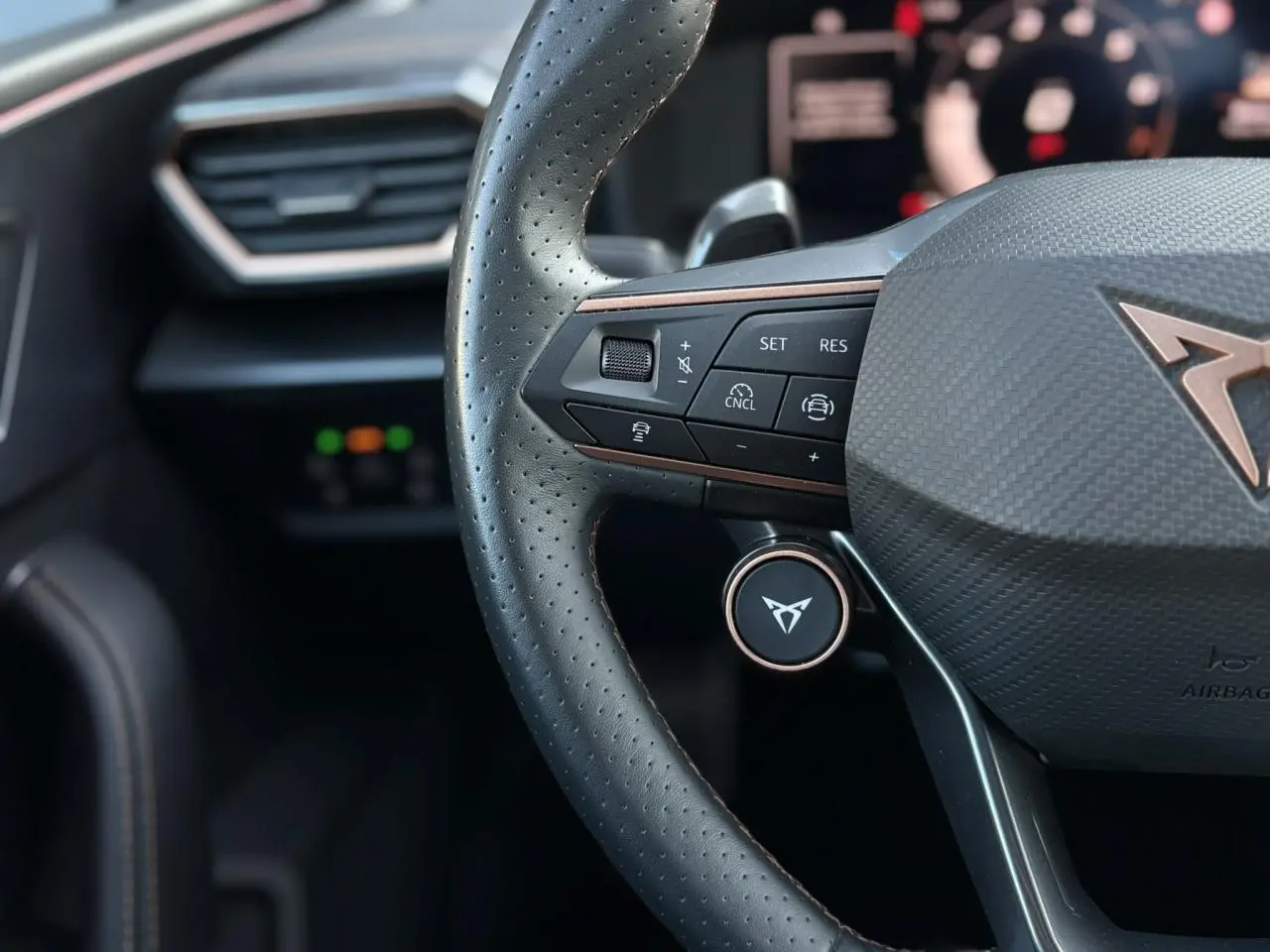 Gros plan sur le volant Supersports noir perforé avec logo CUPRA cuivré et commandes multifonctions visibles.