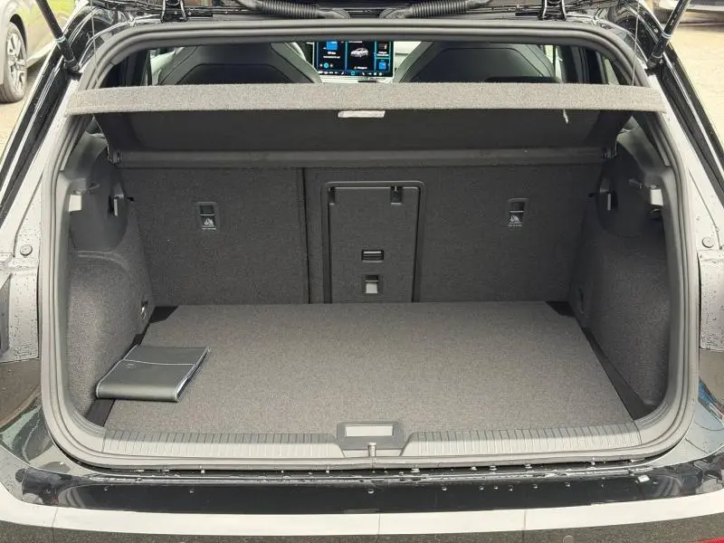Coffre ouvert vu de l'arrière d'une Volkswagen Golf 2.0 TDI 150ch R-Line noire, avec tablette de rangement et banquette arrière rabattable.