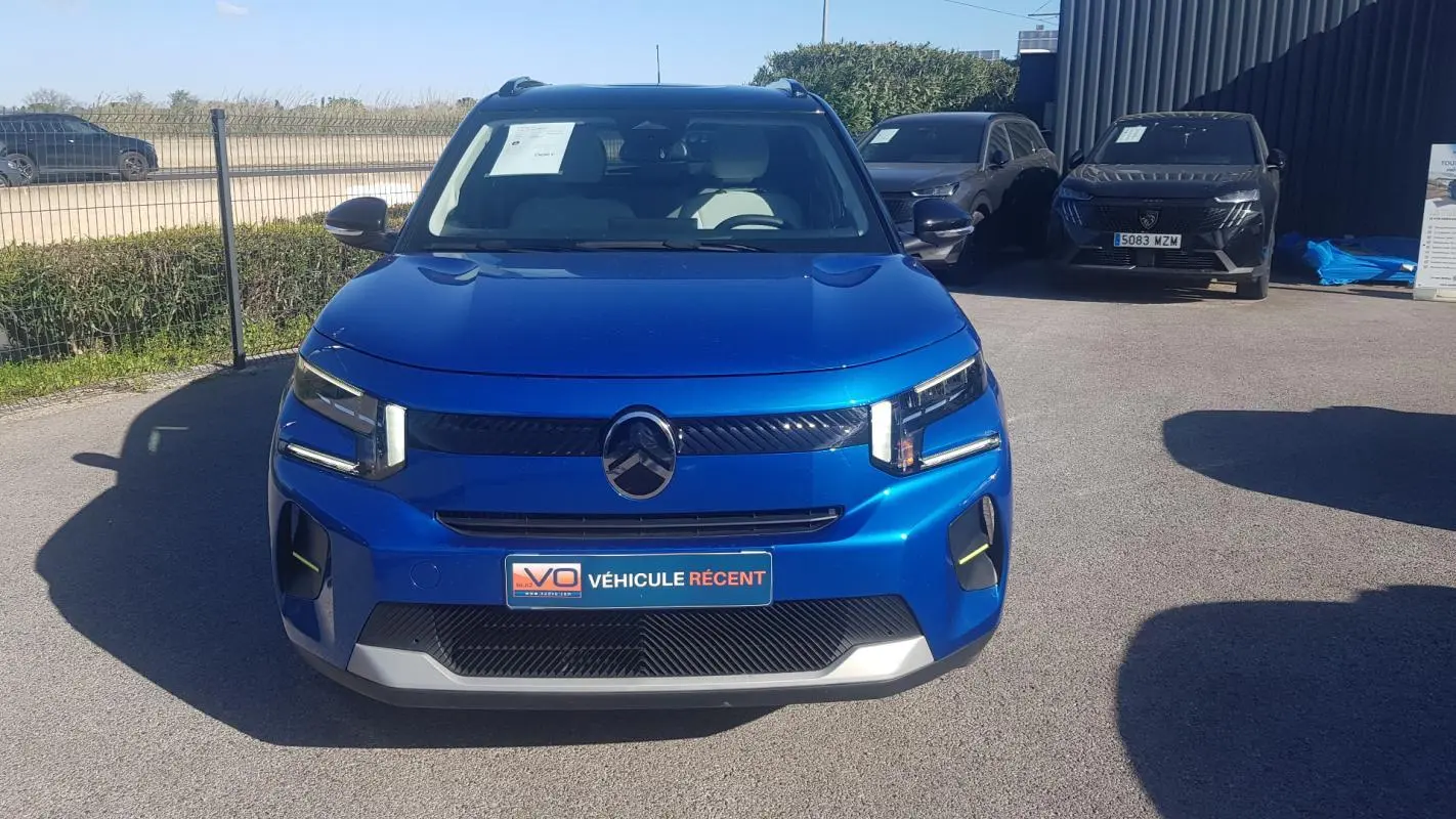 Vue de face d'une Citroën C3 bleu foncé 2024 avec barres de toit et feux LED distinctifs, stationnée en extérieur.