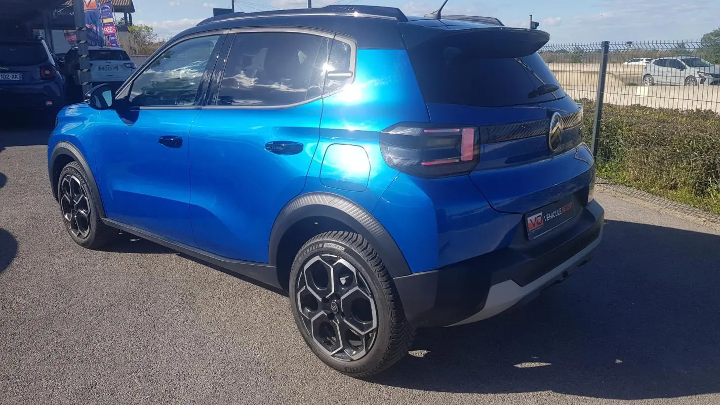 Vue 3/4 arrière droite d'une Citroën C3 2024 bleu foncé avec jantes alliage noires et barres de toit.