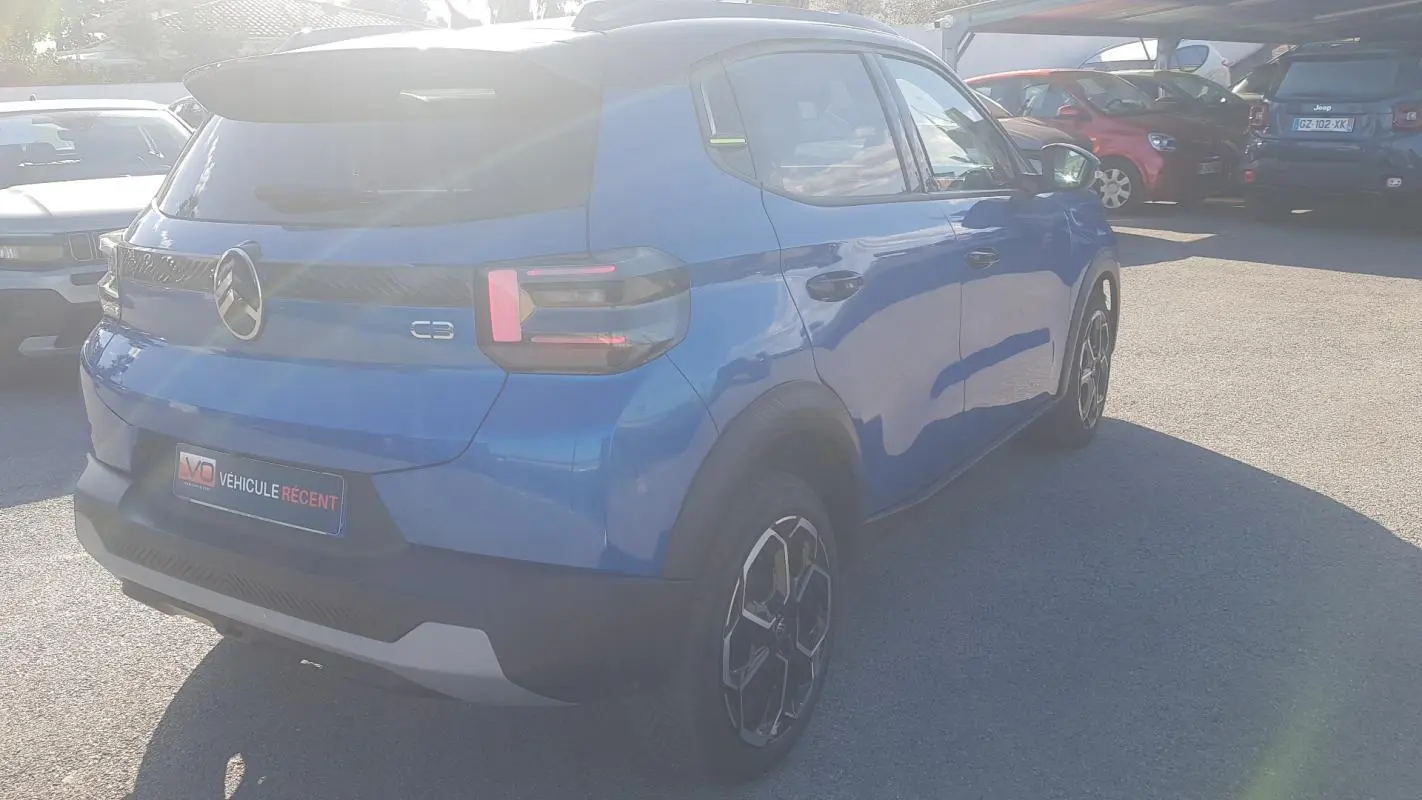 Vue 3/4 arrière droite d'une Citroën C3 bleu foncé 2024 avec jantes alliage et barres de toit visibles.