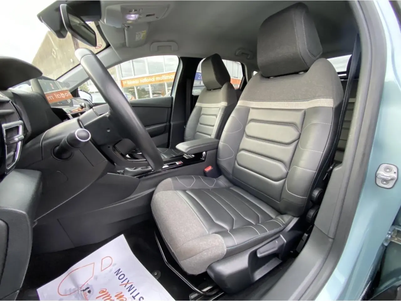 Vue intérieure côté conducteur de la Citroën C4 2021 bleu Iceland, sièges bi-matière gris et noir, tableau de bord visible.