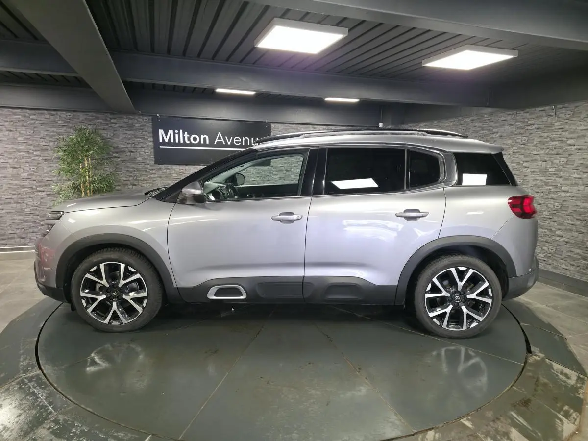 Profil droit d'un Citroën C5 Aircross gris métallisé avec jantes alliage 19 pouces et barres de toit bi-ton.