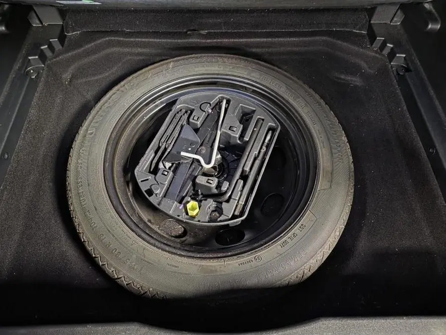 Gros plan sur la roue de secours galette noire et son kit de réparation dans le coffre d'un Citroën C5 Aircross gris.