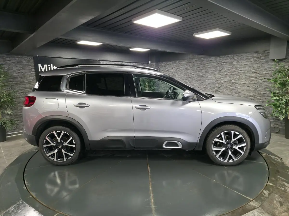 Vue de profil côté gauche d'un Citroën C5 Aircross gris métallisé avec jantes alliage 19 pouces dans un showroom.