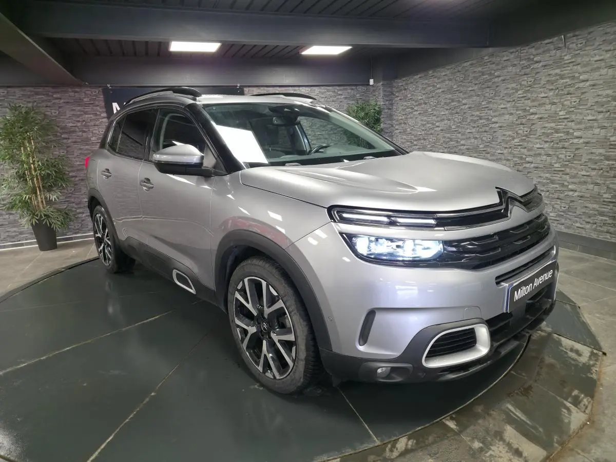Vue 3/4 avant droit d'un Citroën C5 Aircross gris métallisé avec jantes alliage 19 pouces et barres de toit noires.