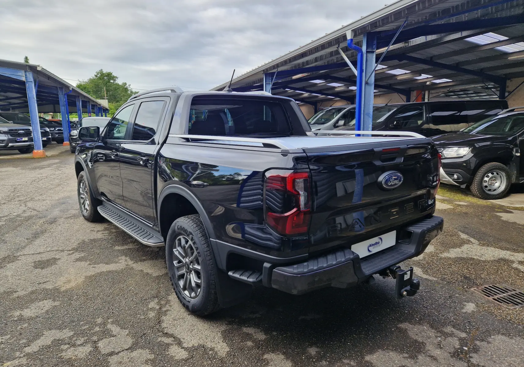 Vue 3/4 arrière droite du Ford Ranger Double Cabine noir 2023 avec rideau de plateau coulissant et marchepied visible.