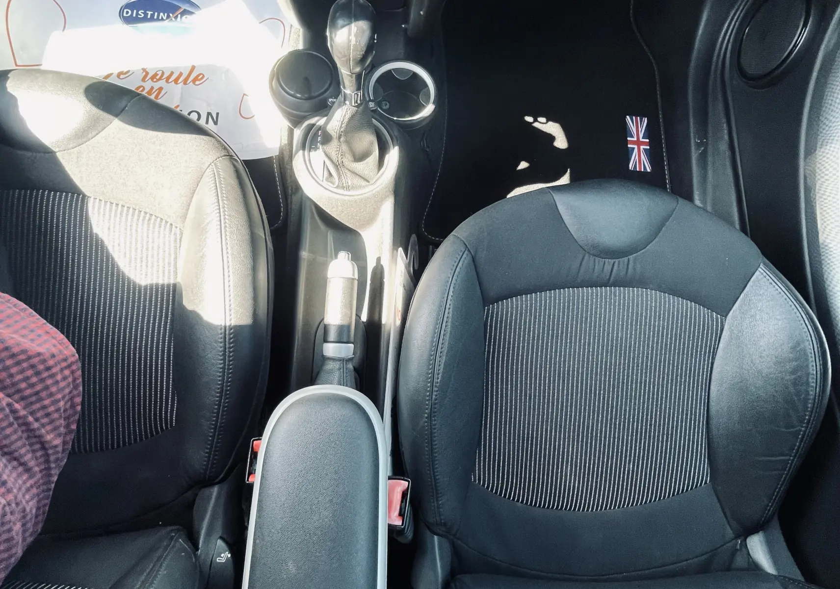 Vue plongeante sur l'intérieur avant noir d'une MINI Cooper S 2008 avec console centrale et sièges en tissu rayé.