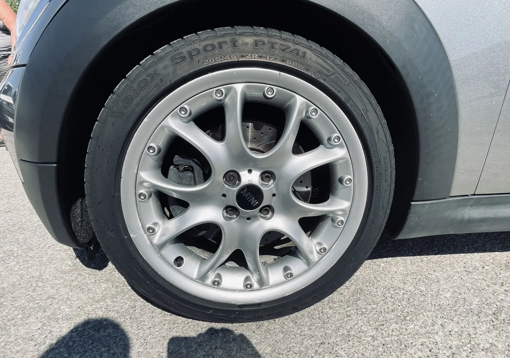 Gros plan sur la roue avant gauche gris clair d'une MINI Cooper S 2008 avec jante alu et logo MINI au centre.