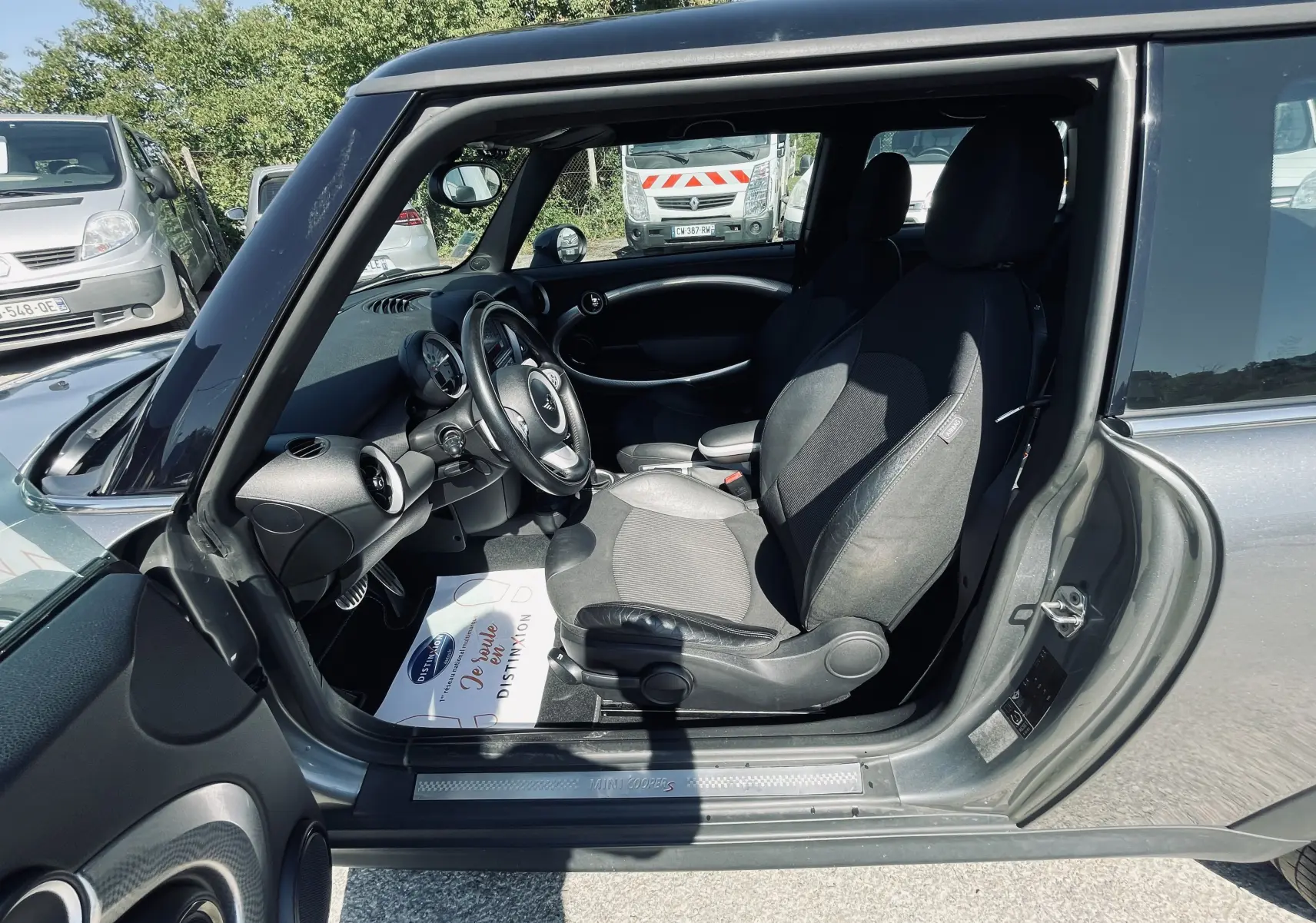 Intérieur côté conducteur d'une MINI Cooper S grise de 2008, avec sièges noirs et tableau de bord visible.