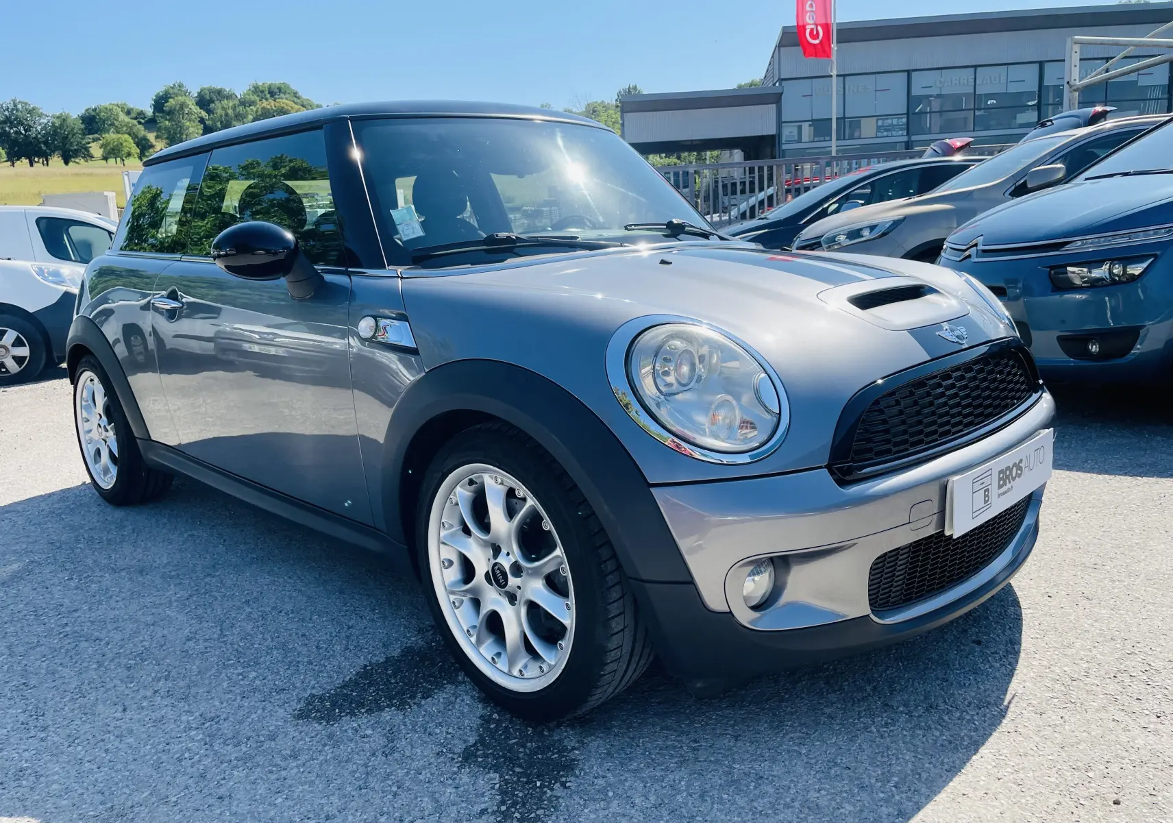 Vue 3/4 avant droite d'une MINI Cooper S grise avec jantes argentées, stationnée en extérieur par temps ensoleillé.