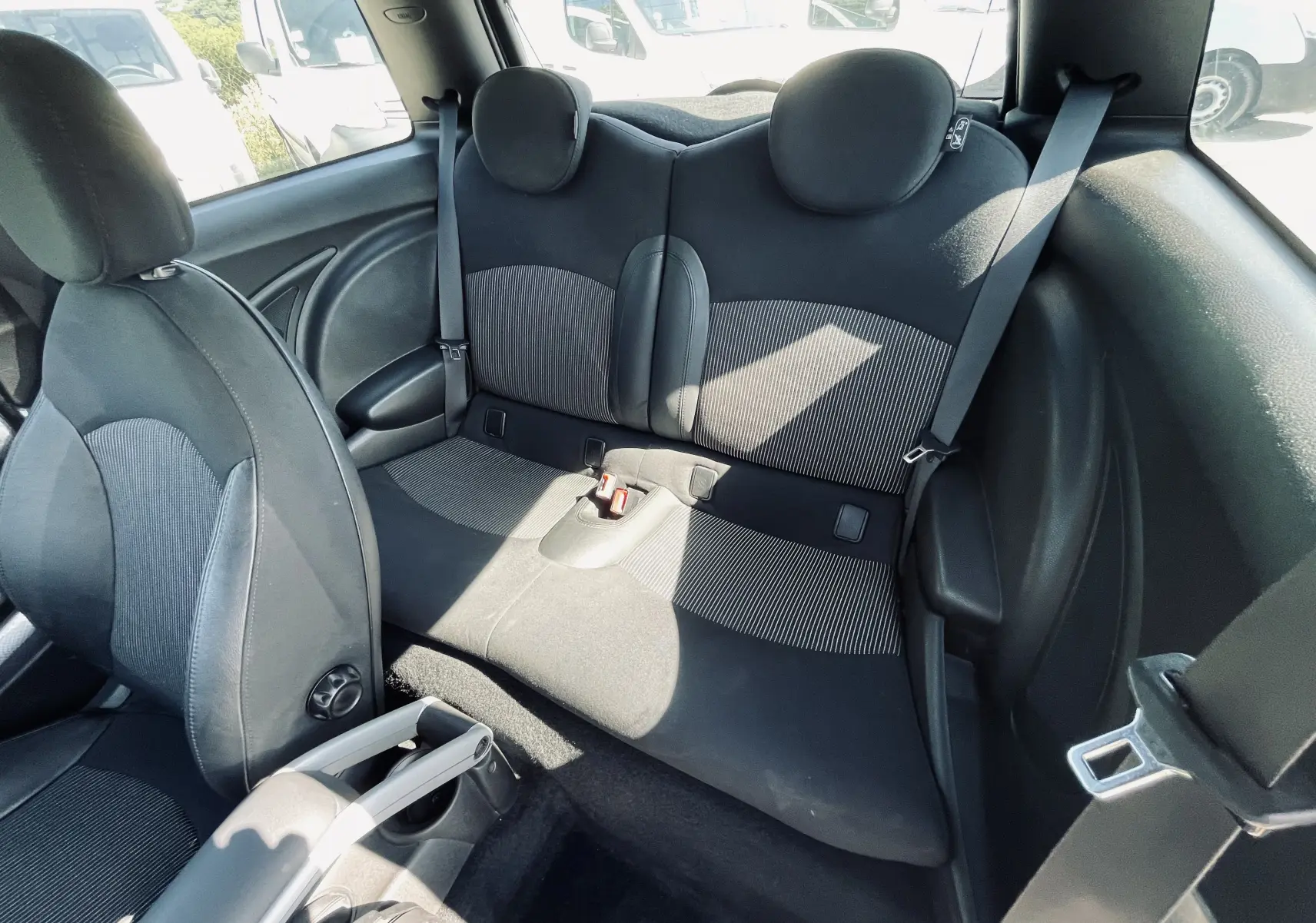 Vue intérieure arrière de la MINI Cooper S 2008 montrant les sièges arrière noirs avec appuie-têtes ronds et ceintures de sécurité.