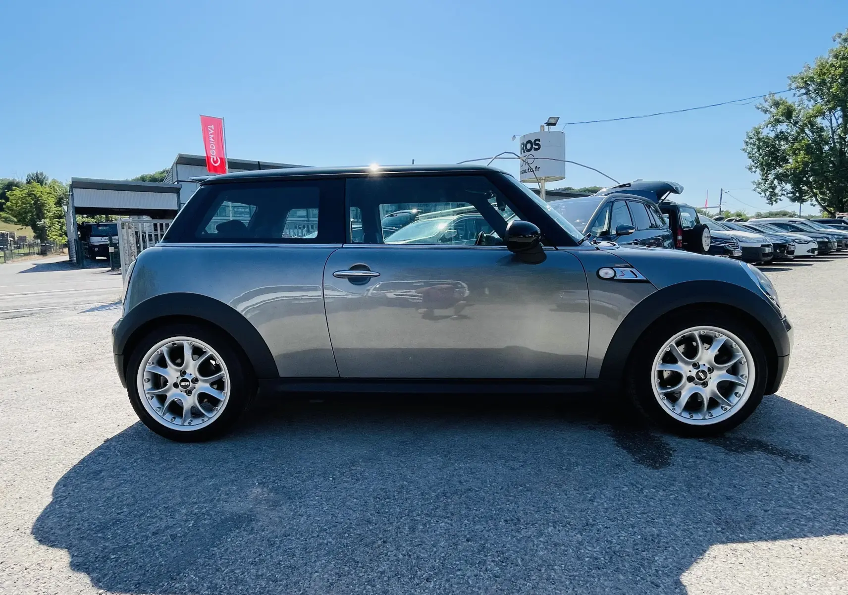 Profil droit d'une MINI Cooper S gris métallisé avec jantes alliage 17 pouces sur un parking ensoleillé.