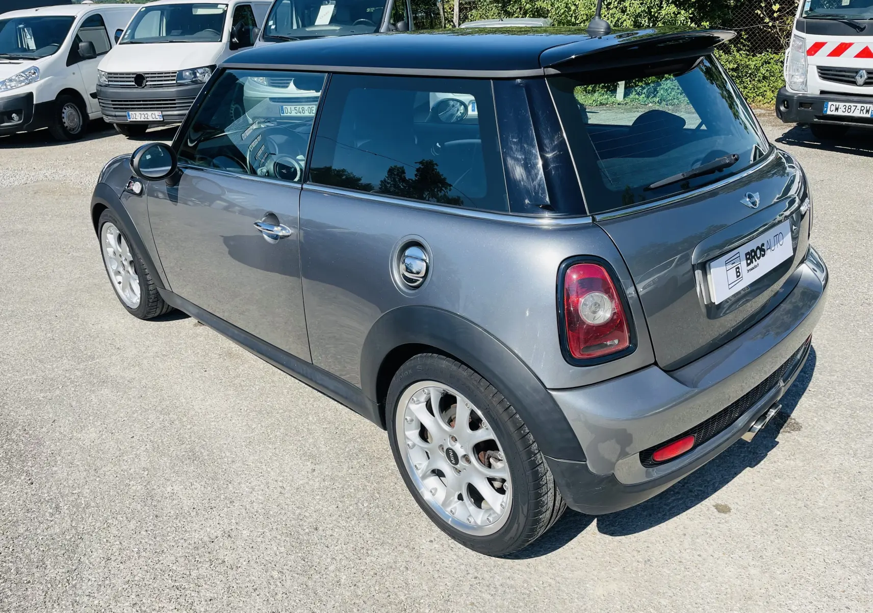 Vue 3/4 arrière droite d'une MINI Cooper S grise avec toit noir et becquet arrière noir sur parking.