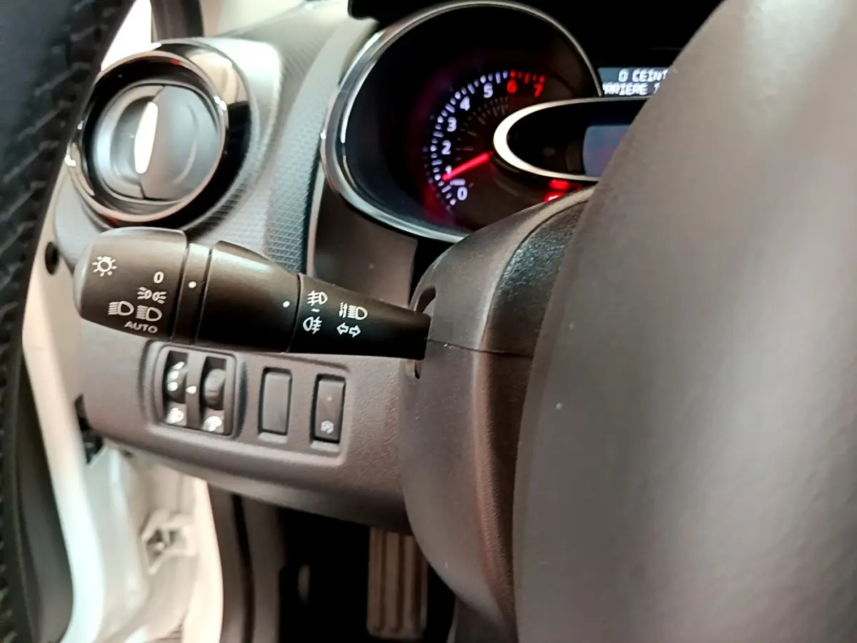 Gros plan sur le commodo gauche et le tableau de bord éclairé d'une Renault Clio Business blanche de 2019.