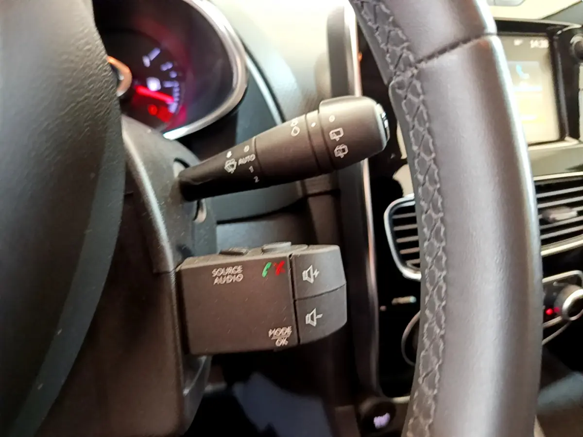 Gros plan sur la commande audio au volant cuir noir d'une Renault Clio Business blanche, tableau de bord et écran tactile en arrière-plan.