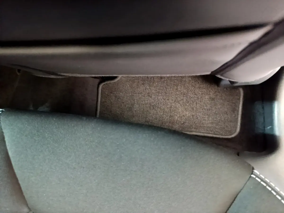 Vue rapprochée du sol côté passager arrière d’une Renault Clio blanche, tapis de sol gris et siège tissu noir.