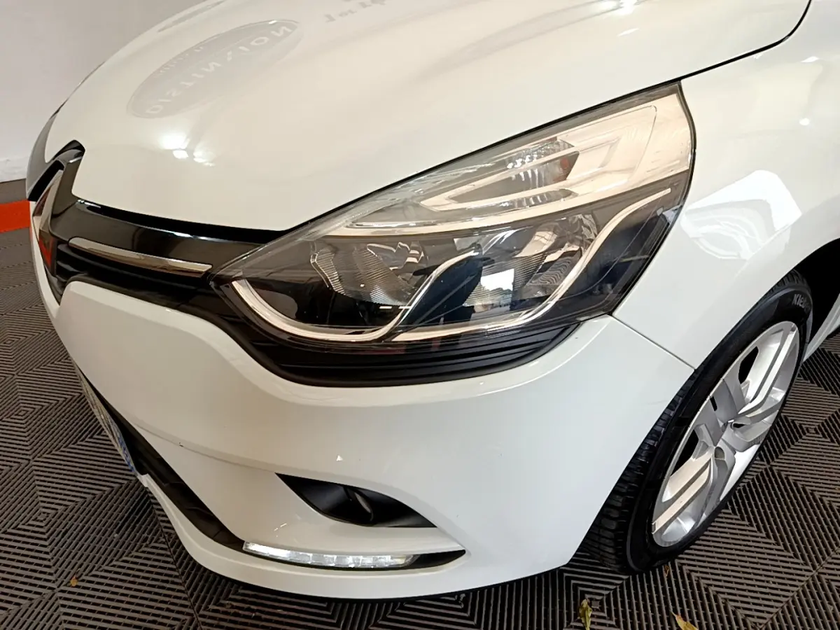Gros plan sur l'avant droit d'une Renault Clio Business TCe 90 blanche, mettant en valeur son phare et la calandre noire brillante.