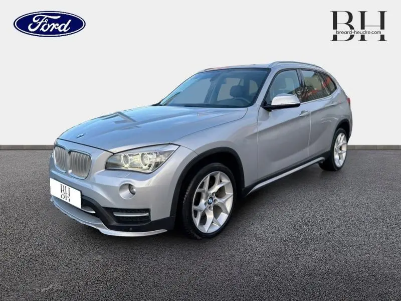 BMW X1 xDrive25dA 2014 en Mineralgrau, vue 3/4 avant droit avec jantes alu et phares bi-xénon allumés