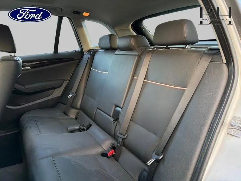 Vue intérieure arrière du BMW X1 xDrive25dA 2014 montrant la banquette en cuir noir avec ceintures de sécurité et appuie-têtes.