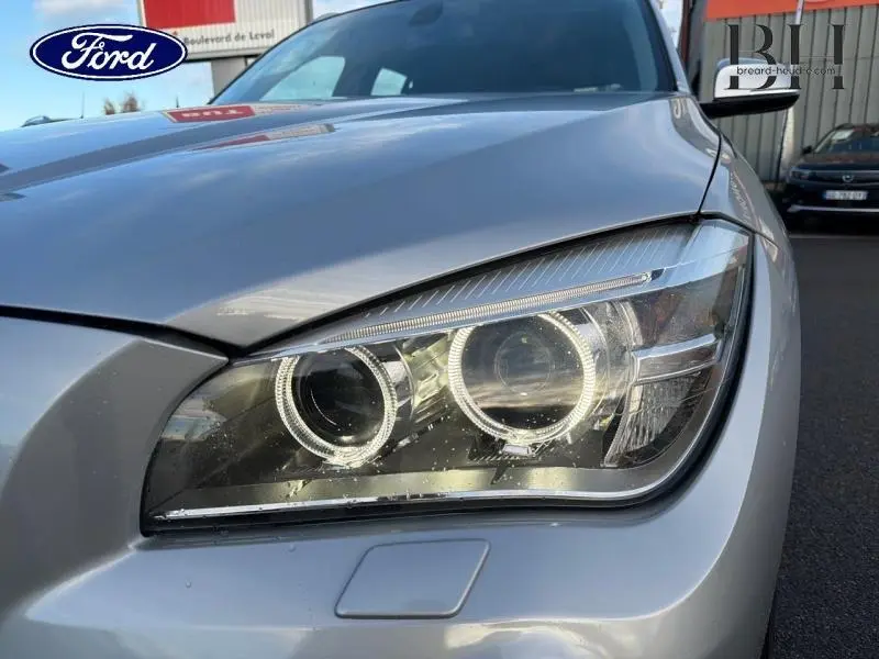 Gros plan sur le phare avant droit d'une BMW X1 xDrive25dA 2014 couleur Mineralgrau avec éclairage LED distinctif.