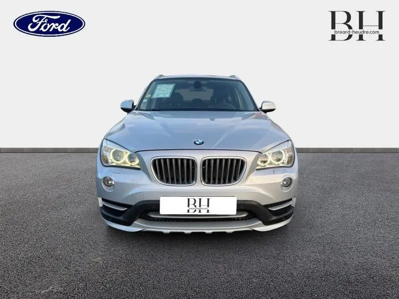 Vue frontale d'un BMW X1 xDrive25dA 2014 en Mineralgrau avec phares allumés et calandre caractéristique double haricot.