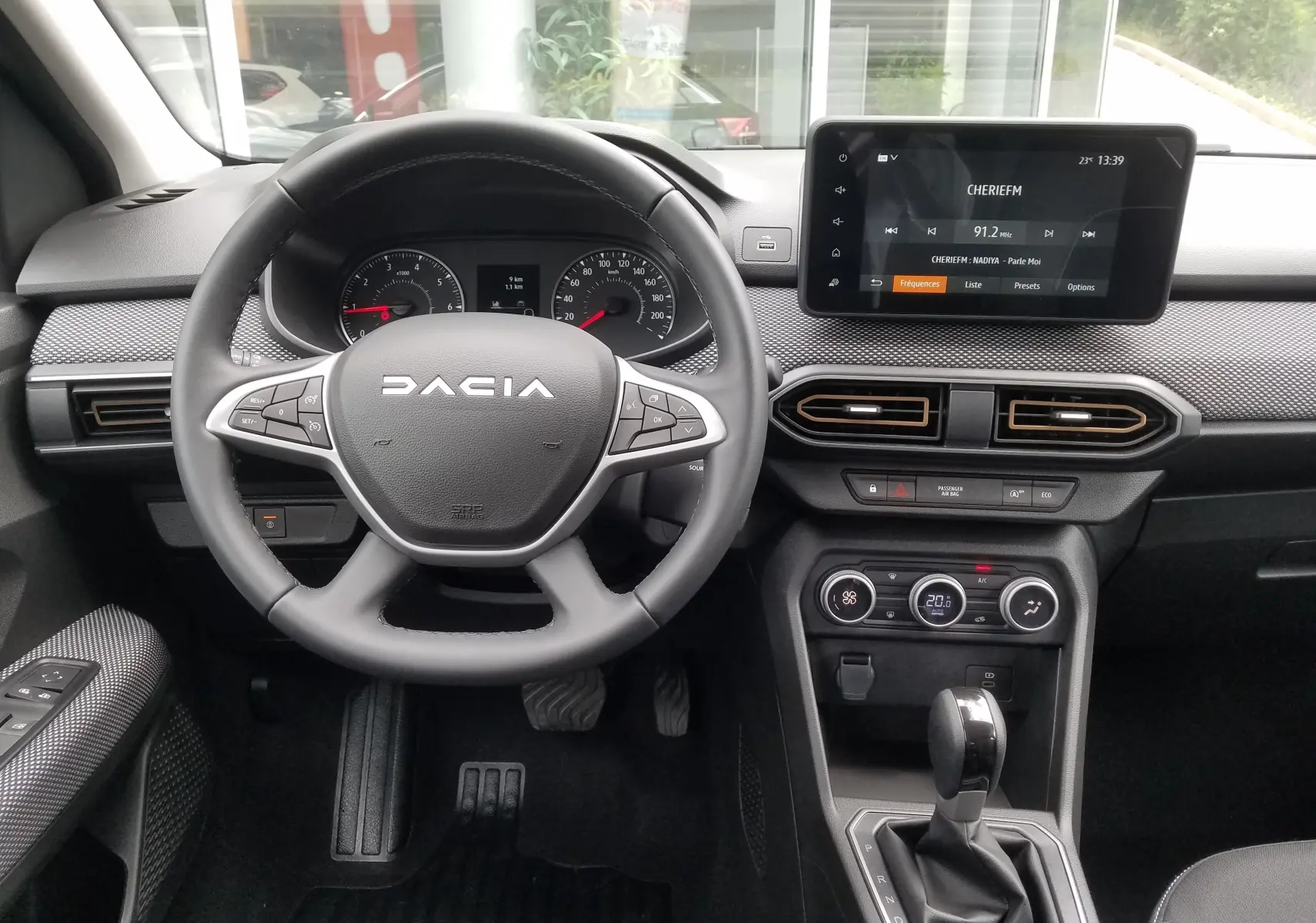 Vue intérieure centrée sur le volant DACIA et le tableau de bord avec écran tactile et commandes de climatisation.