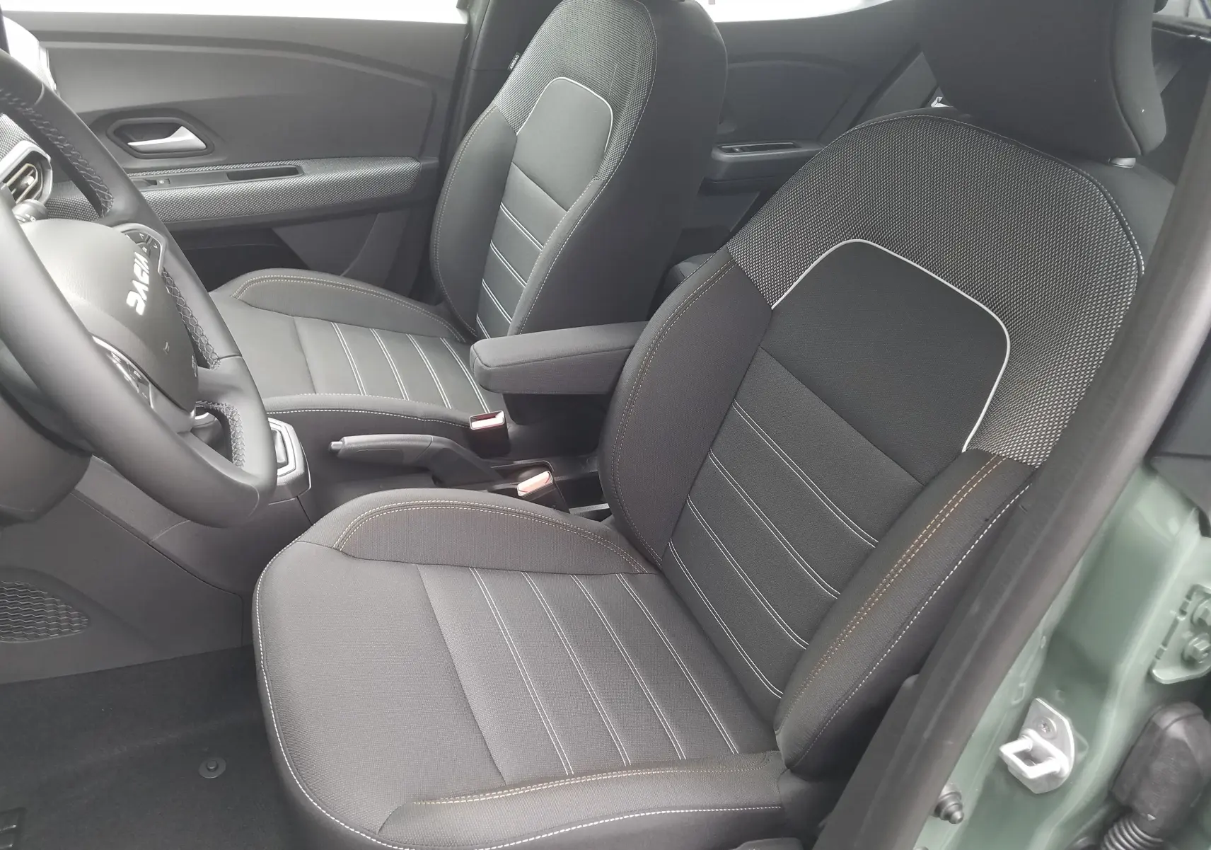 Vue intérieure côté conducteur du Dacia Sandero Stepway 2025 en Licken Kaki, sièges noirs avec surpiqûres contrastantes.