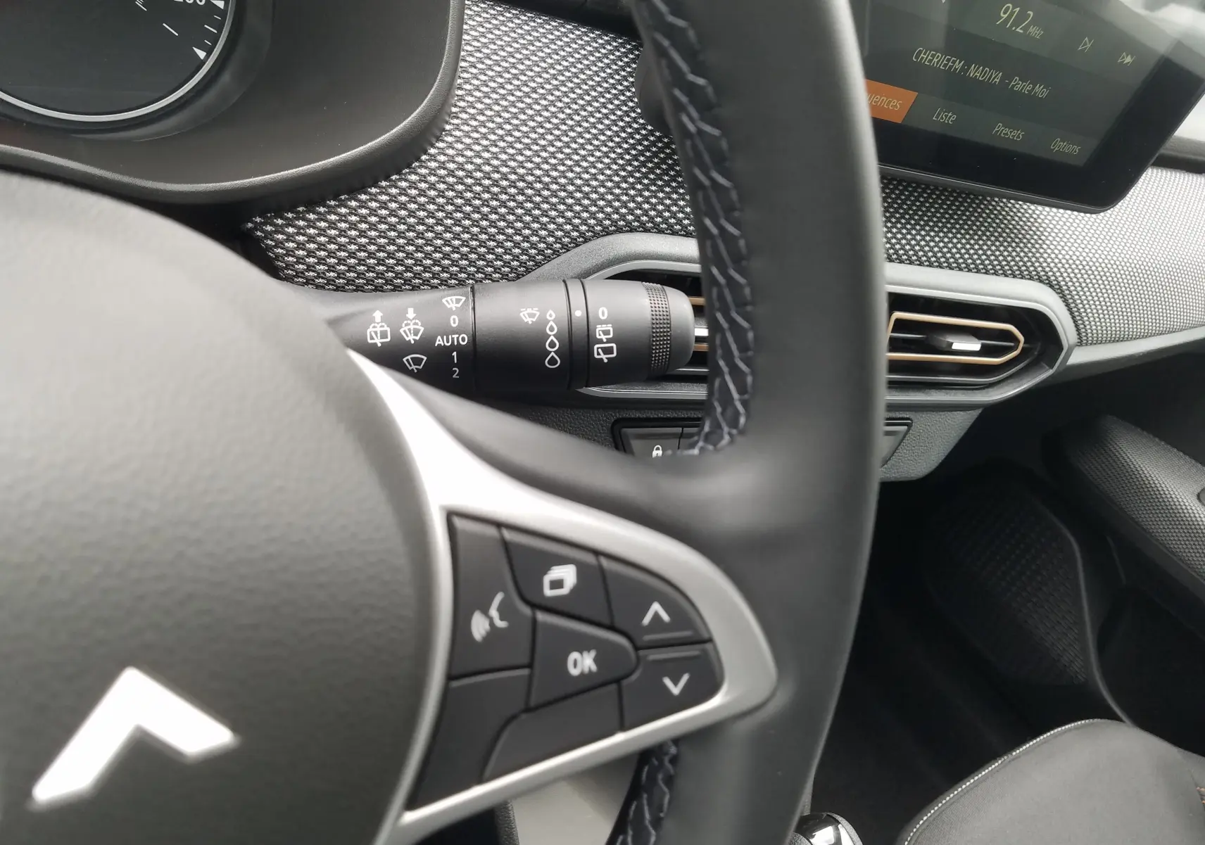 Gros plan sur le volant et la commande d'essuie-glace du tableau de bord du Dacia Sandero Stepway 2025, intérieur noir.