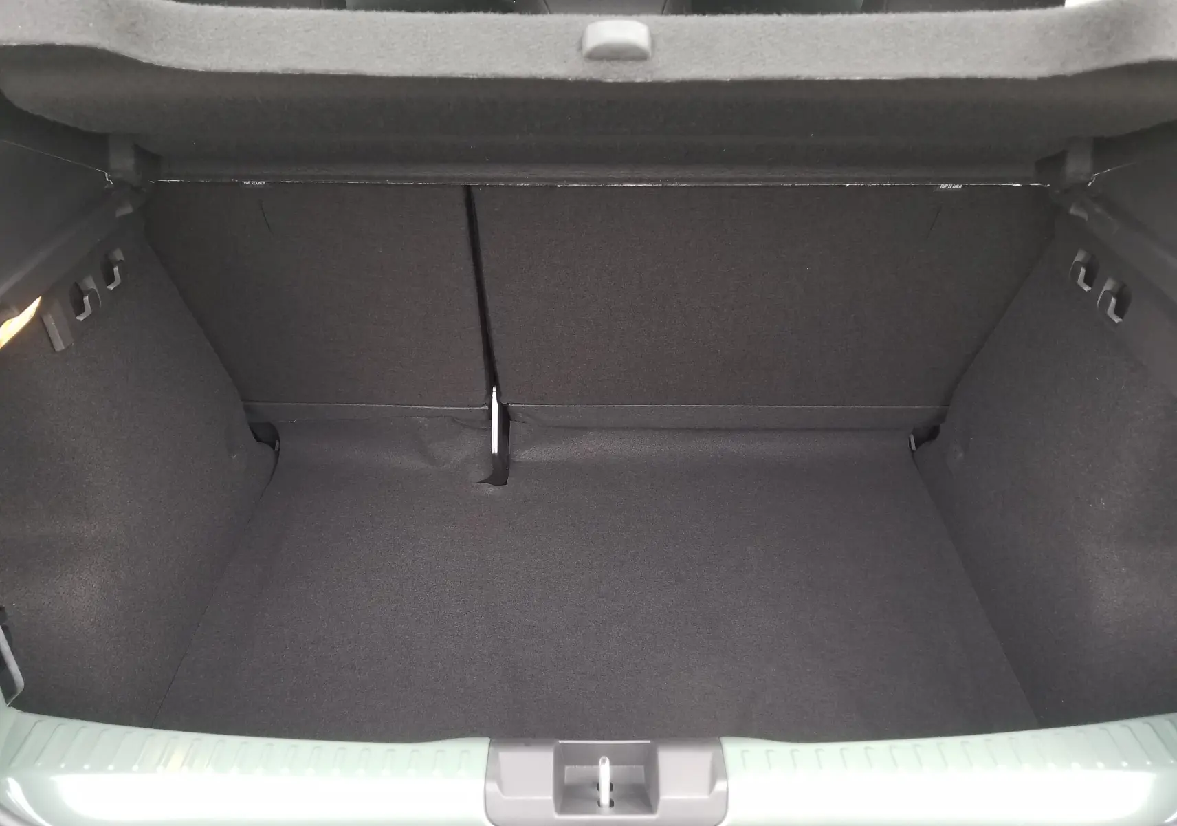 Coffre ouvert vu de l'arrière d'une Dacia Sandero Stepway 2025 en Licken Kaki, intérieur noir et tapis de coffre.