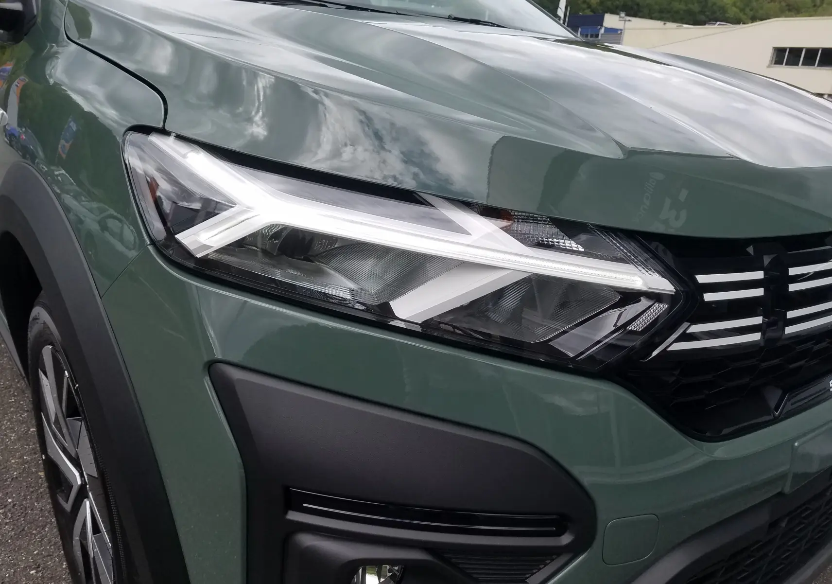 Gros plan sur le phare avant gauche et la calandre noire d'une Dacia Sandero Stepway 2025 en vert Licken Kaki.