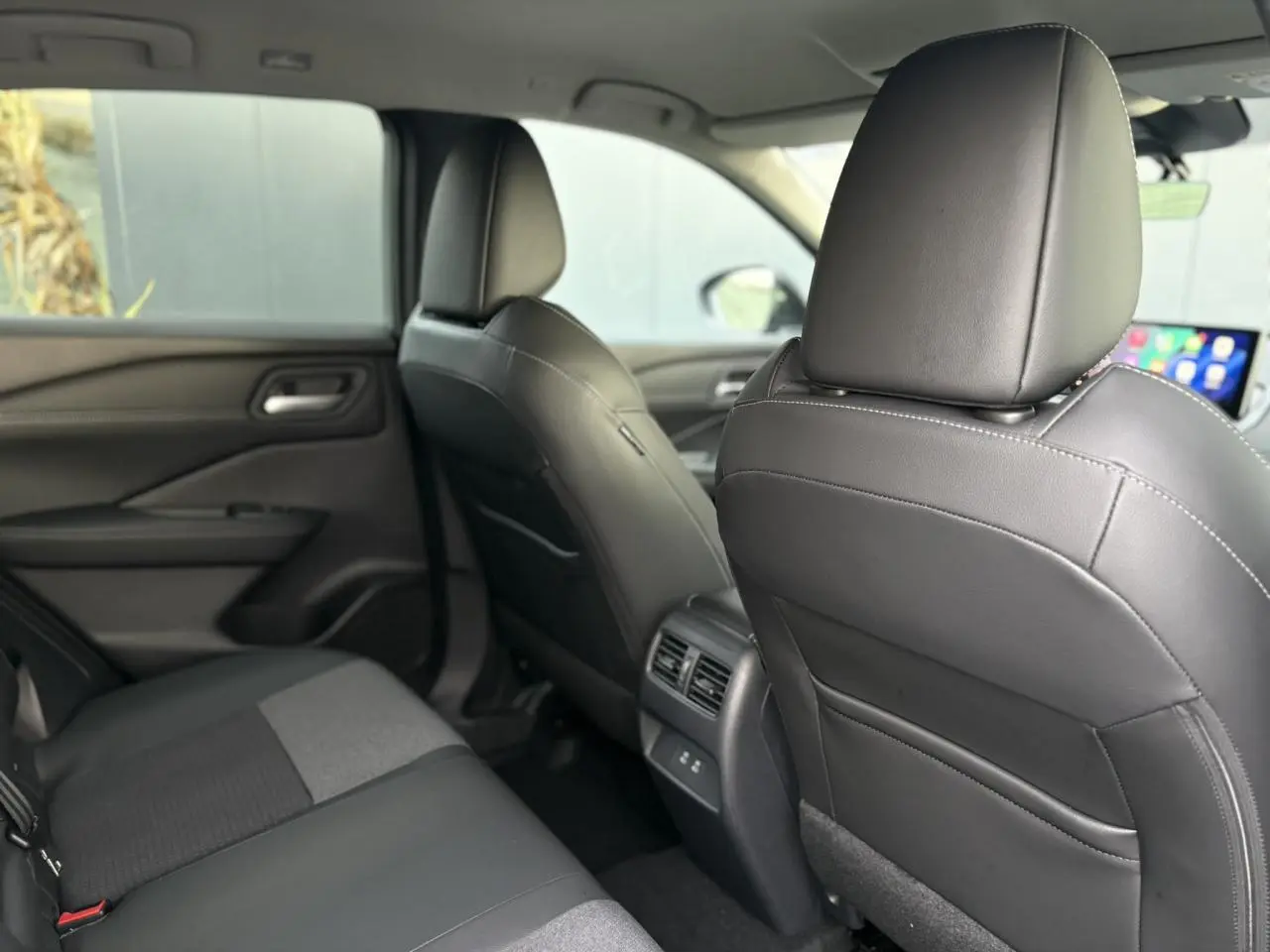 Vue intérieure arrière du Nissan Qashqai 2025, sièges noirs en cuir et tissu avec console centrale et ports USB visibles.