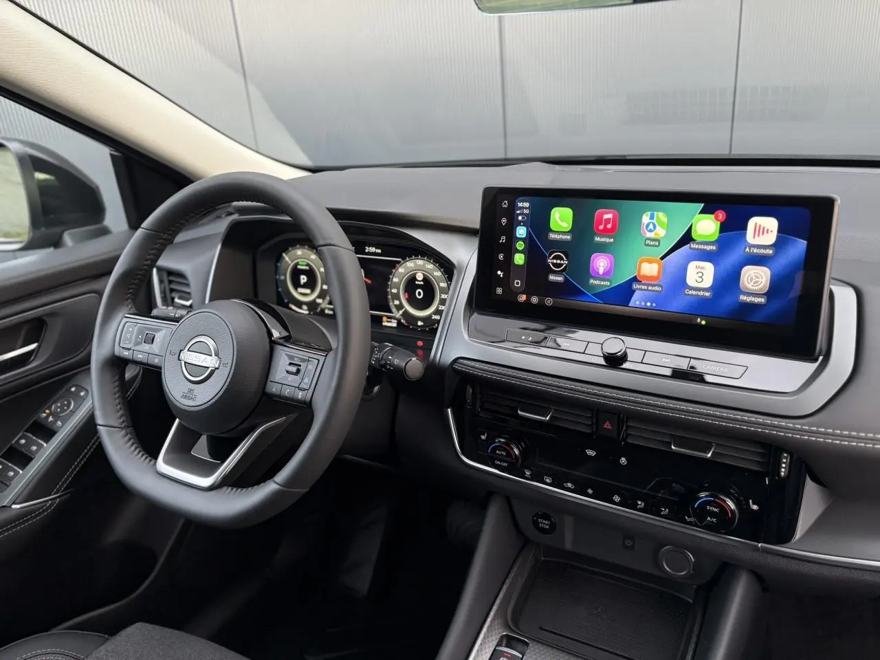 Vue intérieure côté conducteur du Nissan Qashqai gris Ceramic 2025, avec écran tactile large et volant cuir noir.