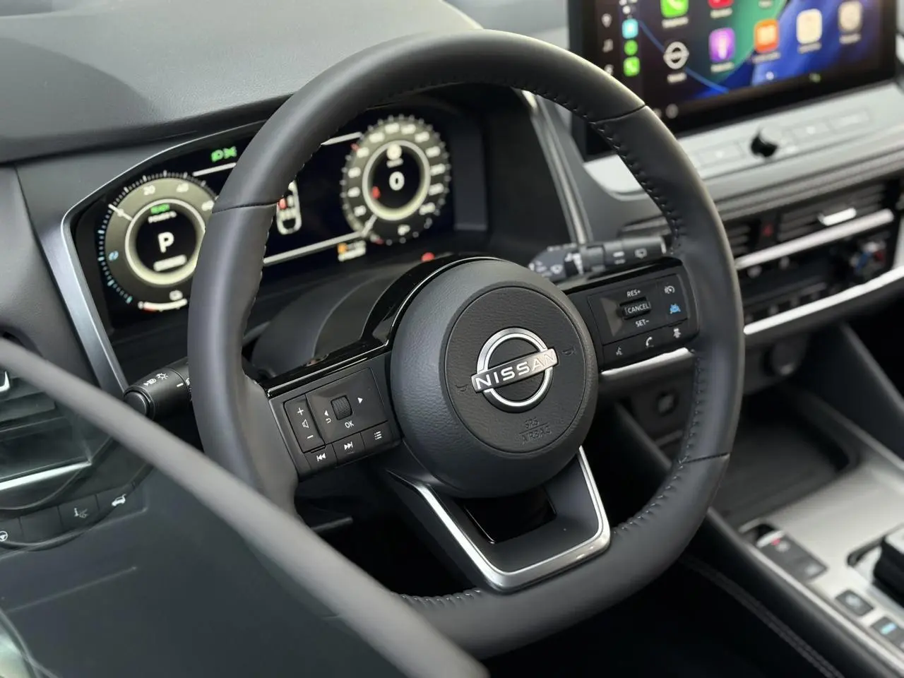 Vue intérieure rapprochée du volant cuir noir du Nissan Qashqai 2025 avec tableau de bord numérique et écran tactile.